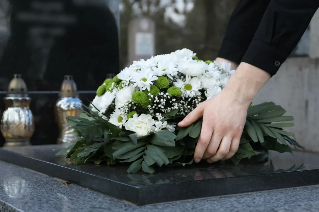 woman putting funeral wreath flowers granite tombstone cemetery closeup